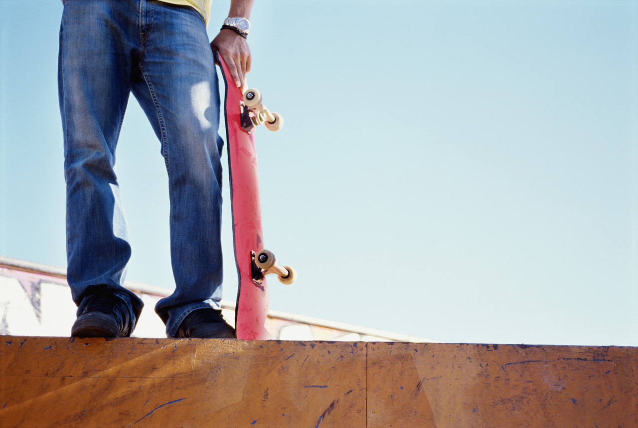 Low section of a male skateboarder holding his skateboard